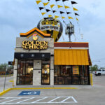 The exterior of the new Golden Chick in Eagle Pass with a Now Open balloon and banner flags above the building.