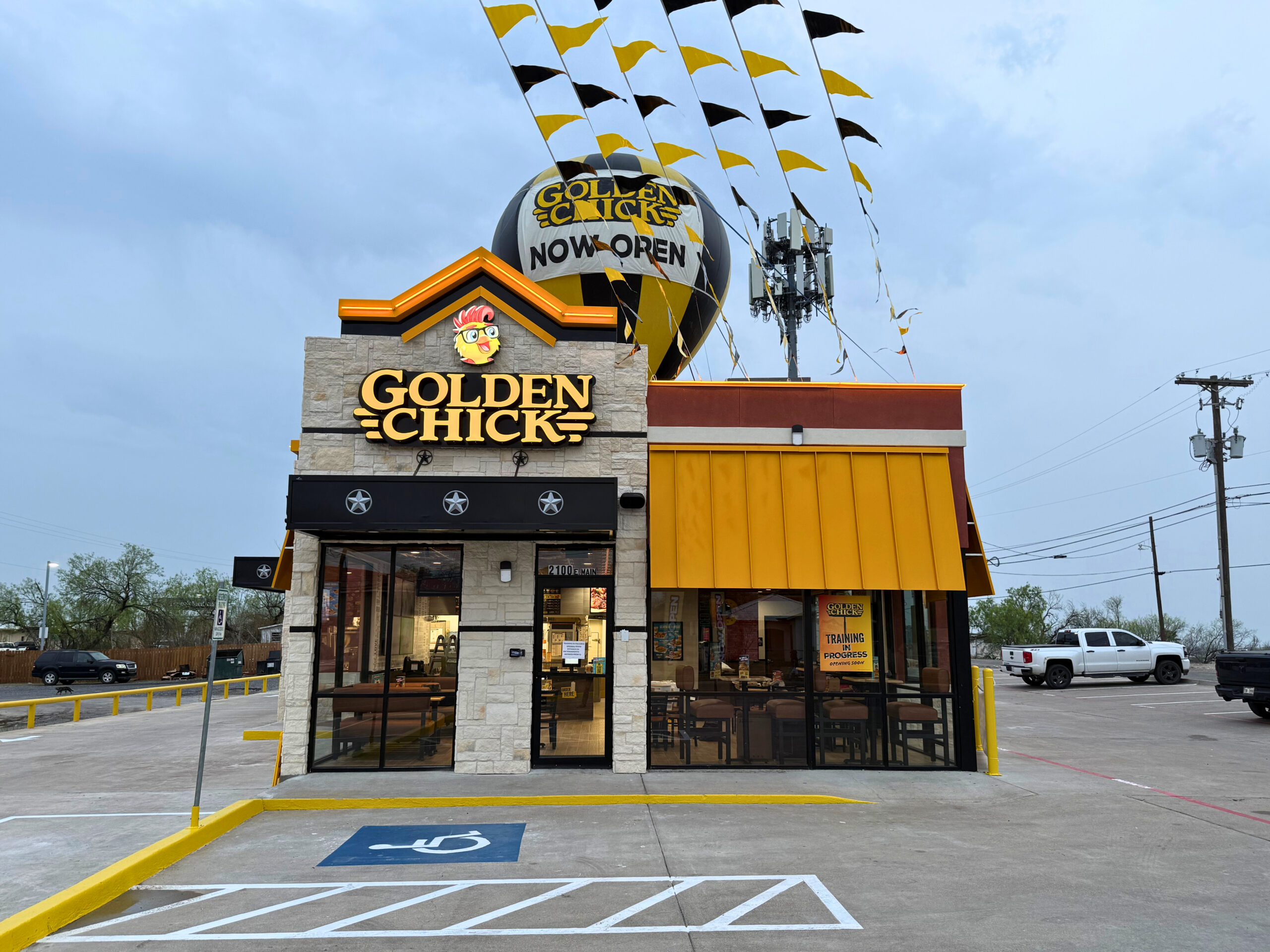 The exterior of the new Golden Chick in Eagle Pass with a Now Open balloon and banner flags above the building.